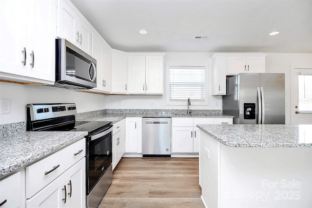 kitchen with light wood finished floors, stainless steel appliances, visible vents, white cabinetry, and a sink