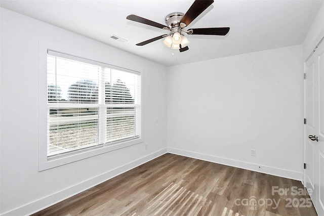 empty room with a ceiling fan, wood finished floors, visible vents, and baseboards