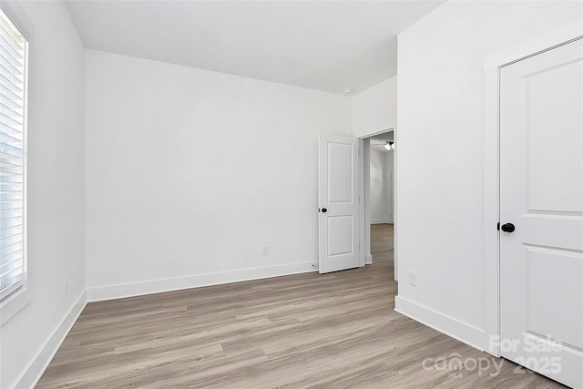 unfurnished bedroom featuring light wood finished floors, multiple windows, and baseboards
