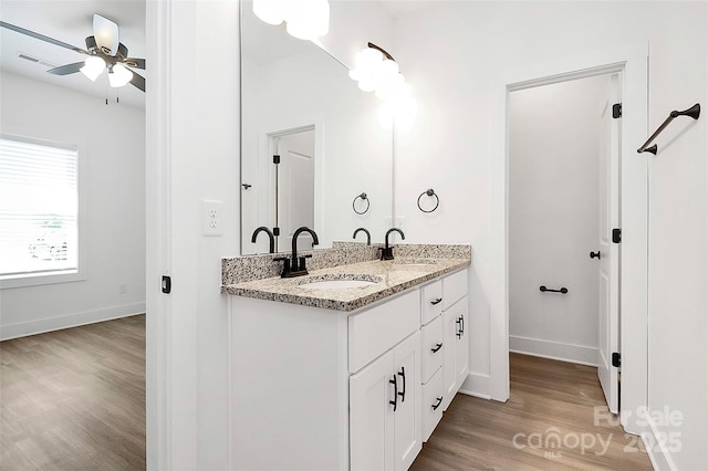 full bath featuring a ceiling fan, wood finished floors, a sink, double vanity, and baseboards