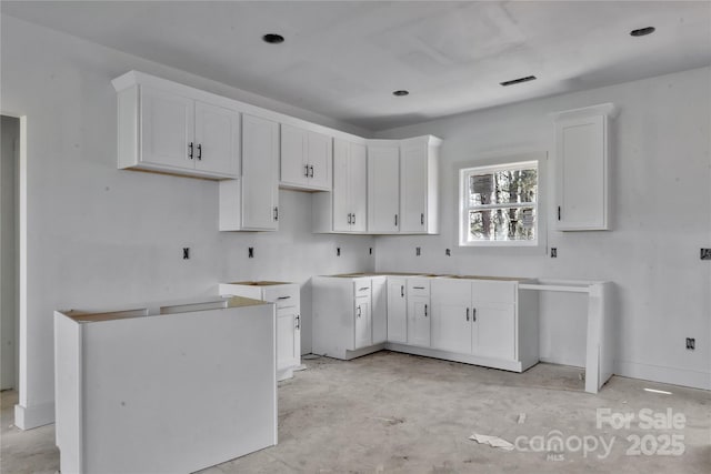 kitchen featuring concrete flooring, white cabinetry, visible vents, and baseboards