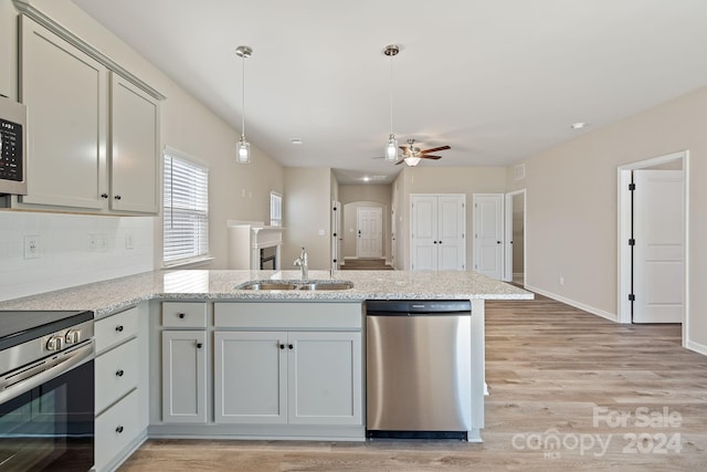 kitchen with kitchen peninsula, stainless steel appliances, ceiling fan, sink, and light hardwood / wood-style floors