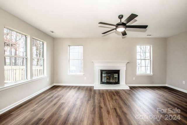 unfurnished living room with a fireplace, ceiling fan, dark wood-type flooring, and a healthy amount of sunlight