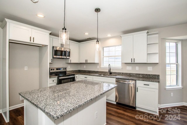 kitchen with appliances with stainless steel finishes, a kitchen island, sink, decorative light fixtures, and white cabinetry