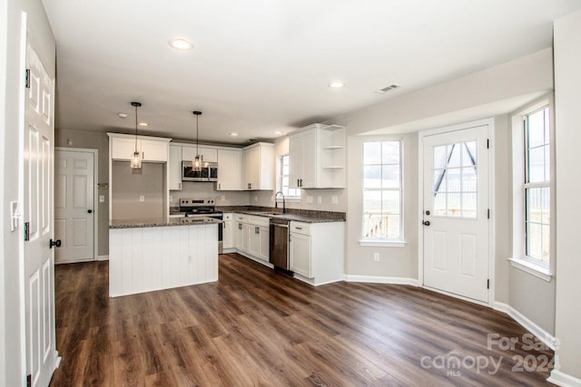 kitchen featuring appliances with stainless steel finishes, a kitchen island, dark hardwood / wood-style floors, white cabinetry, and hanging light fixtures