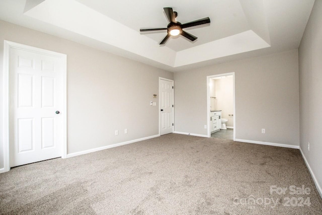 unfurnished bedroom featuring carpet flooring, a raised ceiling, ensuite bath, and ceiling fan