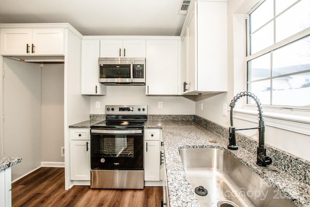 kitchen with sink, appliances with stainless steel finishes, white cabinetry, light stone countertops, and dark hardwood / wood-style flooring