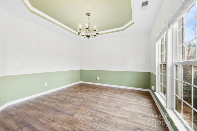 empty room with an inviting chandelier, wood-type flooring, and a raised ceiling