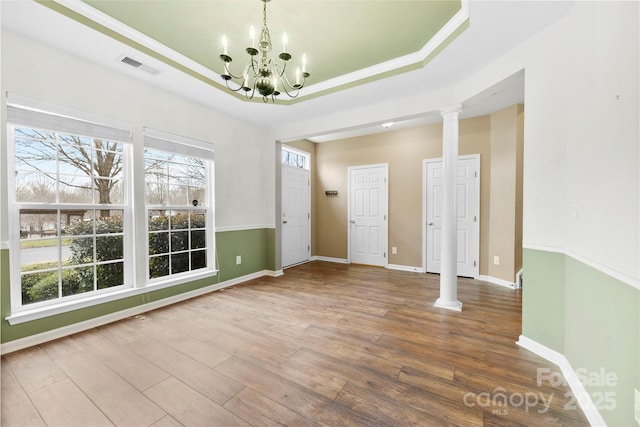 unfurnished room with wood-type flooring, a tray ceiling, decorative columns, and a notable chandelier