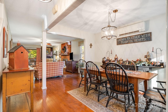 dining room with a wall mounted AC, ceiling fan with notable chandelier, dark wood-type flooring, and a textured ceiling