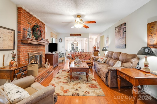 living room featuring light wood-type flooring, a textured ceiling, a fireplace, and ceiling fan