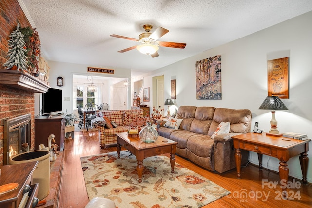 living room with ceiling fan, a fireplace, light wood-type flooring, and a textured ceiling