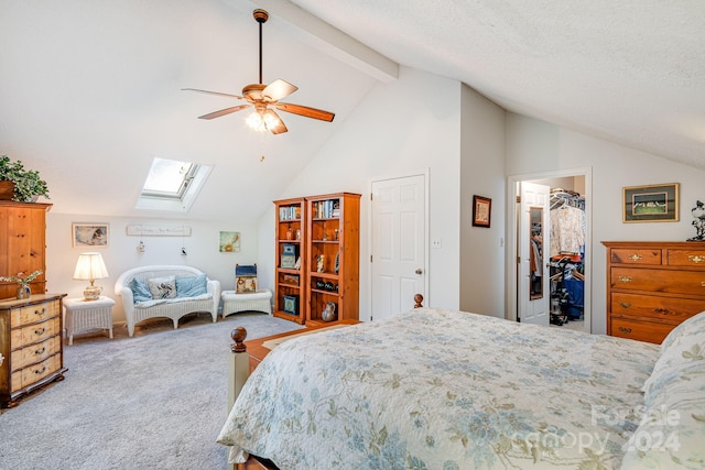 carpeted bedroom with high vaulted ceiling, a walk in closet, a skylight, ceiling fan, and beam ceiling