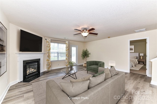 living area featuring a fireplace with flush hearth, light wood-style floors, a textured ceiling, and a ceiling fan