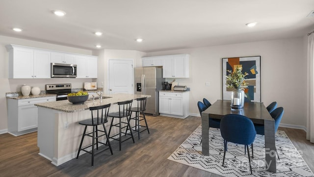 kitchen with white cabinetry, dark wood-type flooring, a breakfast bar area, a kitchen island with sink, and appliances with stainless steel finishes