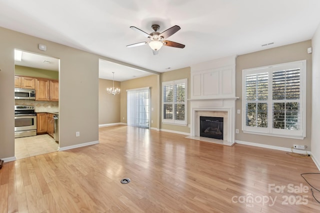 unfurnished living room featuring ceiling fan with notable chandelier, light hardwood / wood-style flooring, and a fireplace