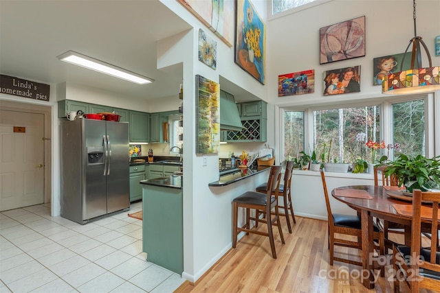 kitchen featuring a breakfast bar area, stainless steel fridge with ice dispenser, kitchen peninsula, green cabinetry, and sink