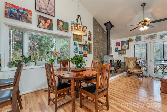 dining room featuring ceiling fan, light hardwood / wood-style floors, french doors, and a wood stove