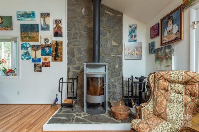 sitting room featuring lofted ceiling, wood-type flooring, and a wood stove