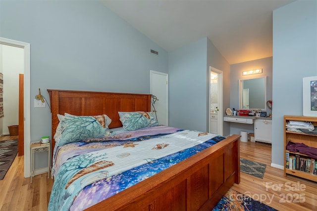 bedroom featuring light wood-type flooring, ensuite bathroom, and vaulted ceiling