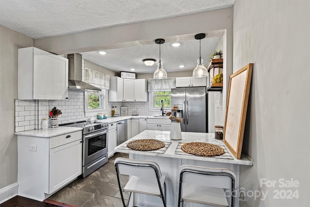 kitchen with wall chimney exhaust hood, pendant lighting, a textured ceiling, white cabinets, and appliances with stainless steel finishes