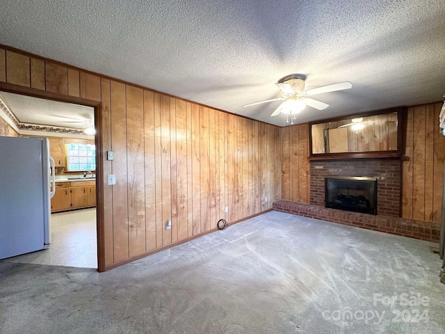 unfurnished living room with a textured ceiling, ceiling fan, a fireplace, and light carpet