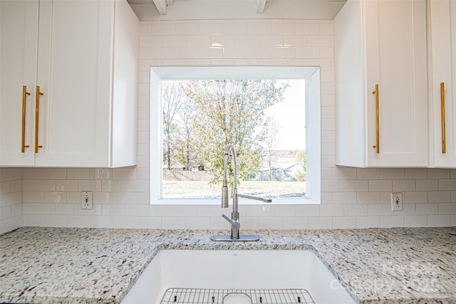 kitchen with white cabinetry, light stone counters, and tasteful backsplash