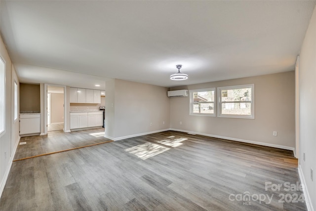 unfurnished living room featuring a wall mounted air conditioner and light hardwood / wood-style floors