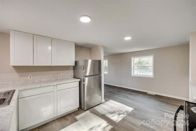 kitchen featuring light wood-type flooring, white cabinetry, stainless steel refrigerator, and sink