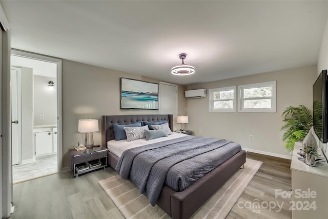 bedroom with light wood-type flooring, a wall unit AC, and connected bathroom