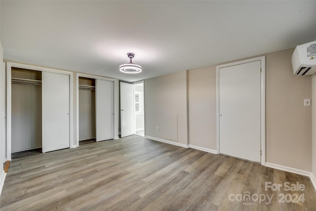 unfurnished bedroom featuring two closets, light hardwood / wood-style flooring, and an AC wall unit