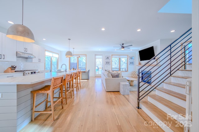 living room with light wood-type flooring, ceiling fan, a healthy amount of sunlight, and sink