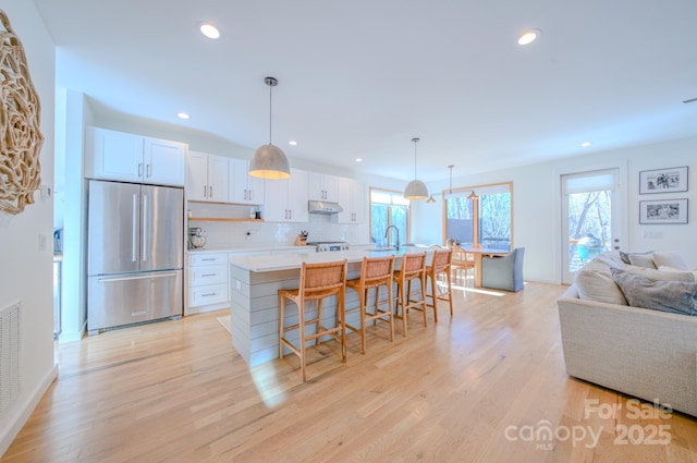 kitchen with backsplash, white cabinetry, high end fridge, and an island with sink