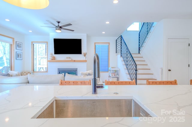 kitchen with ceiling fan, a large fireplace, light stone countertops, and sink