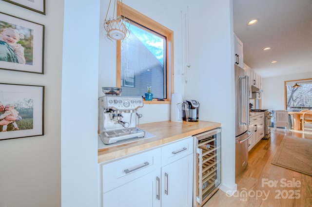 bar featuring high quality appliances, white cabinets, beverage cooler, and decorative light fixtures