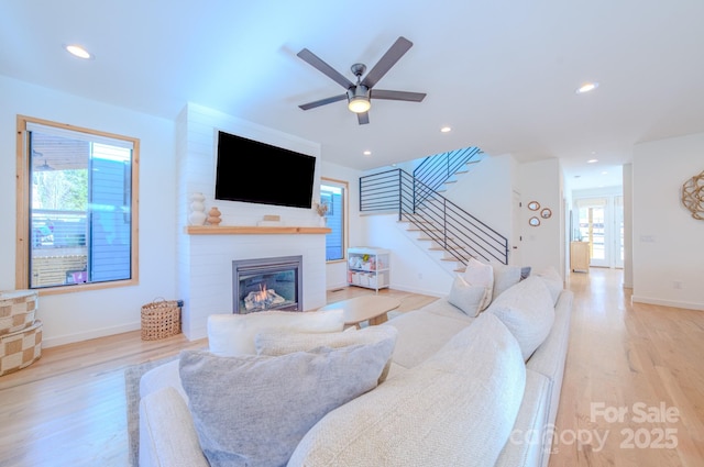 living room featuring a large fireplace, light hardwood / wood-style floors, and ceiling fan