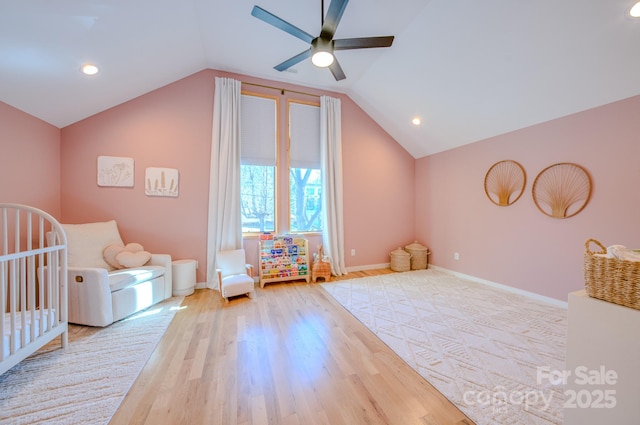 bedroom with ceiling fan, lofted ceiling, light wood-type flooring, and a nursery area