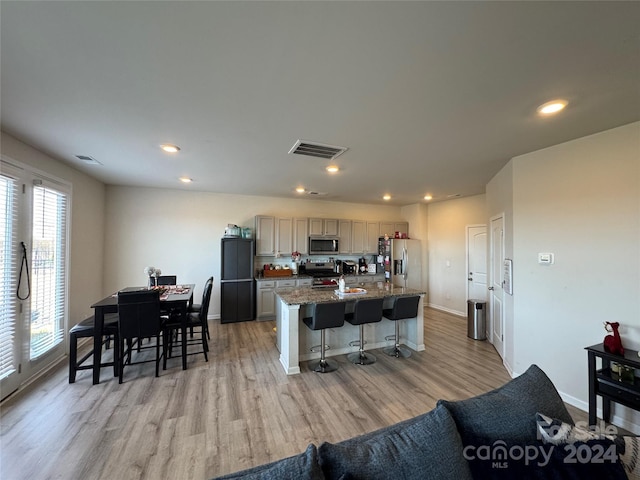 kitchen with a breakfast bar, a kitchen island with sink, dark stone countertops, light hardwood / wood-style floors, and stainless steel appliances