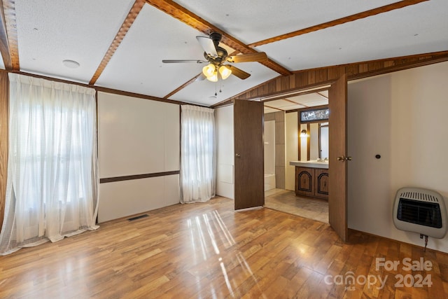 unfurnished bedroom featuring heating unit, lofted ceiling with beams, light hardwood / wood-style floors, and multiple windows