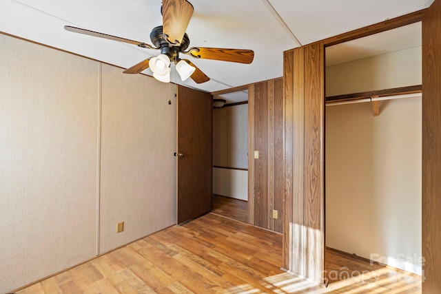 unfurnished bedroom featuring wood walls, ceiling fan, light hardwood / wood-style floors, and a closet