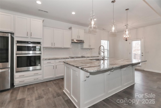 kitchen featuring pendant lighting, white cabinets, a center island with sink, sink, and stainless steel double oven