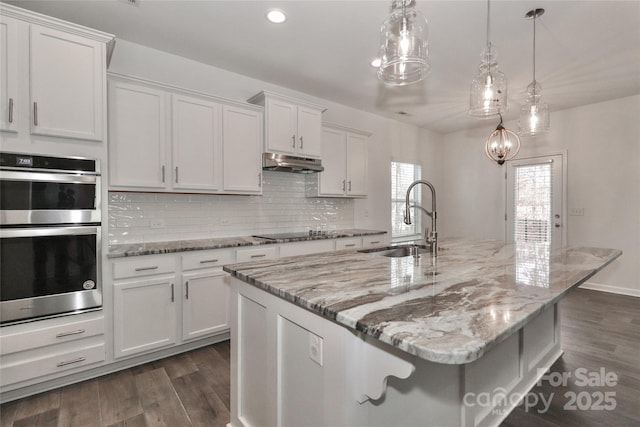 kitchen featuring white cabinets, stainless steel double oven, and a kitchen island with sink