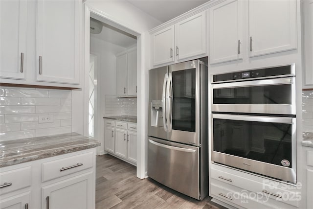 kitchen featuring appliances with stainless steel finishes, tasteful backsplash, light hardwood / wood-style floors, light stone counters, and white cabinetry