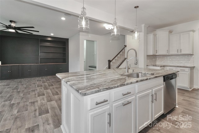 kitchen featuring stainless steel dishwasher, sink, white cabinets, and an island with sink