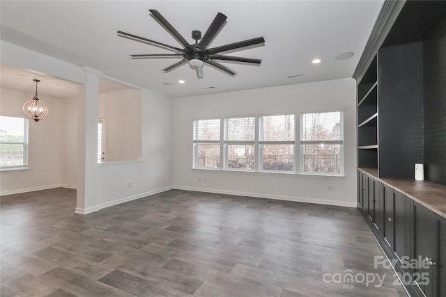 unfurnished living room with ceiling fan with notable chandelier and dark wood-type flooring