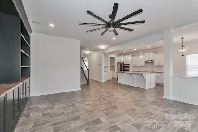 unfurnished living room with ceiling fan with notable chandelier, sink, and light hardwood / wood-style flooring