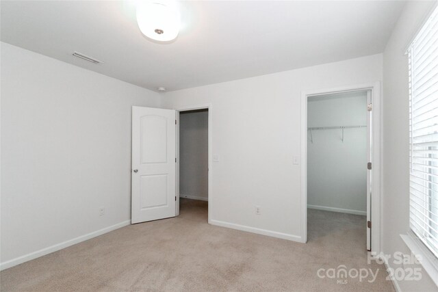 unfurnished bedroom featuring a walk in closet, light carpet, and a closet