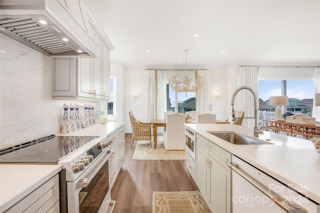 kitchen with pendant lighting, custom exhaust hood, sink, light hardwood / wood-style floors, and stainless steel appliances