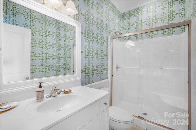 bathroom featuring vanity, toilet, a shower with shower door, and ornamental molding