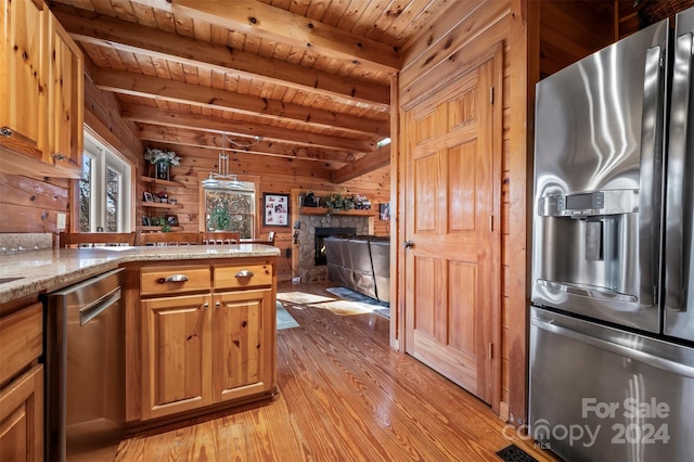 kitchen featuring stainless steel appliances, a stone fireplace, light hardwood / wood-style floors, decorative light fixtures, and wooden walls